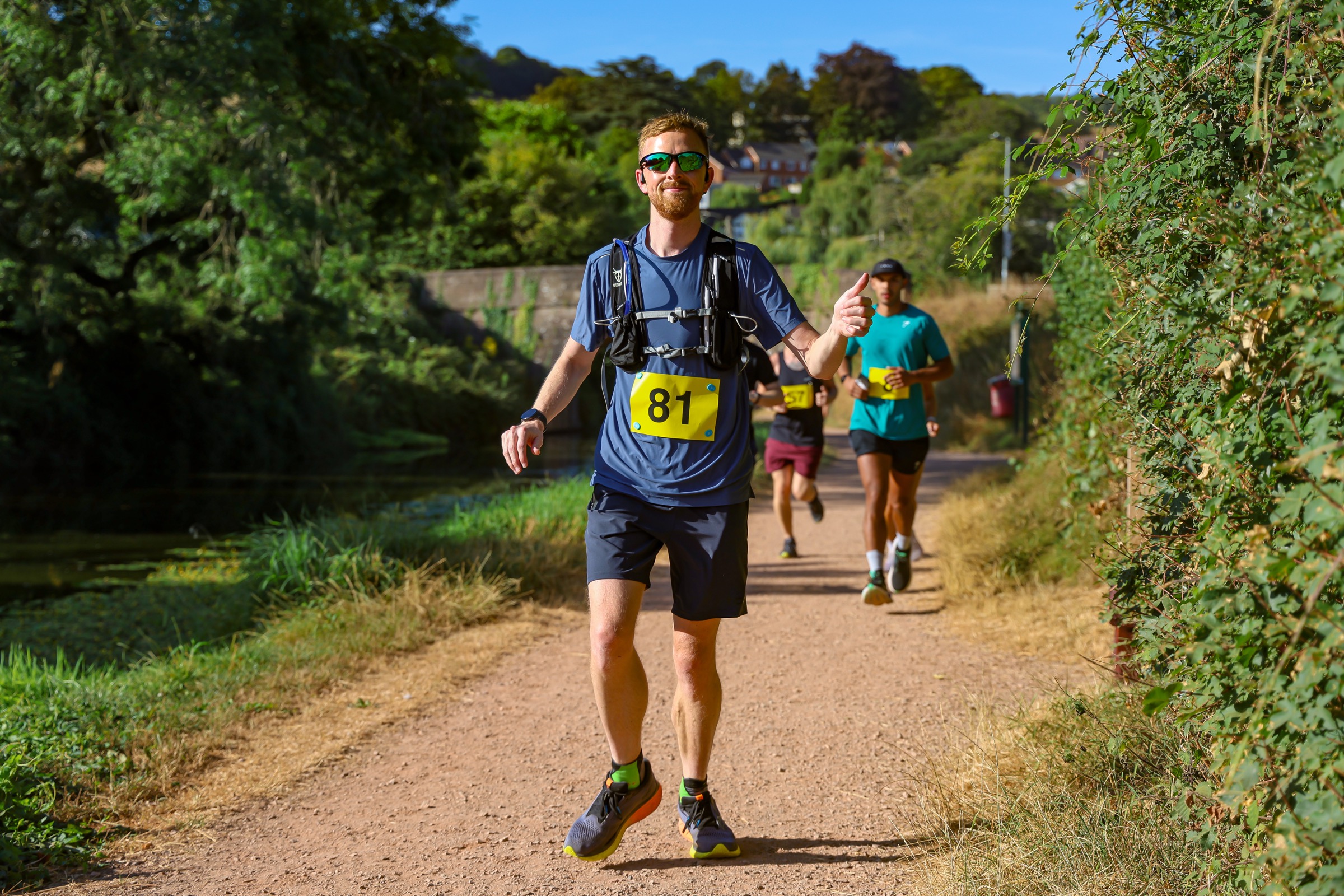 Elliot giving a thumbs-up while running beside the canal at the Tiverton Canal Canter